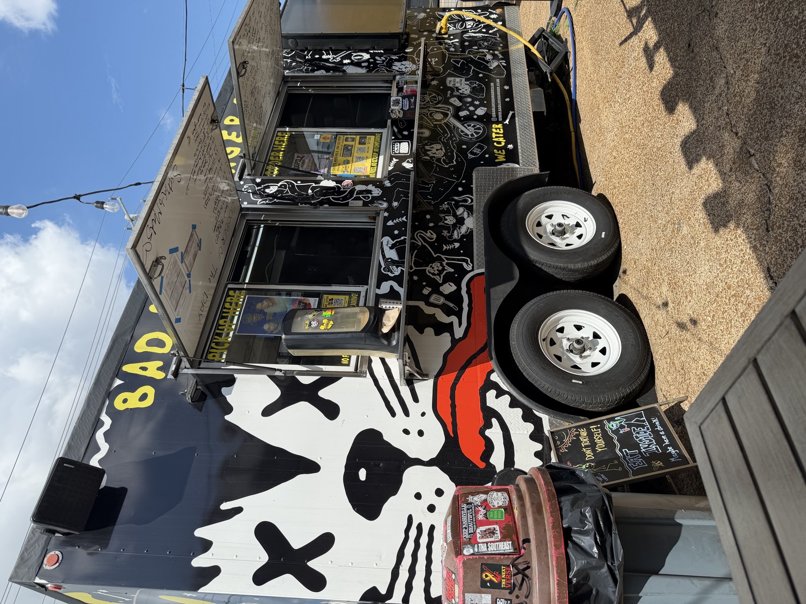 The order window side of the Bad Luck Burger Club trailer, with a big cat mural and a chalkboard sign