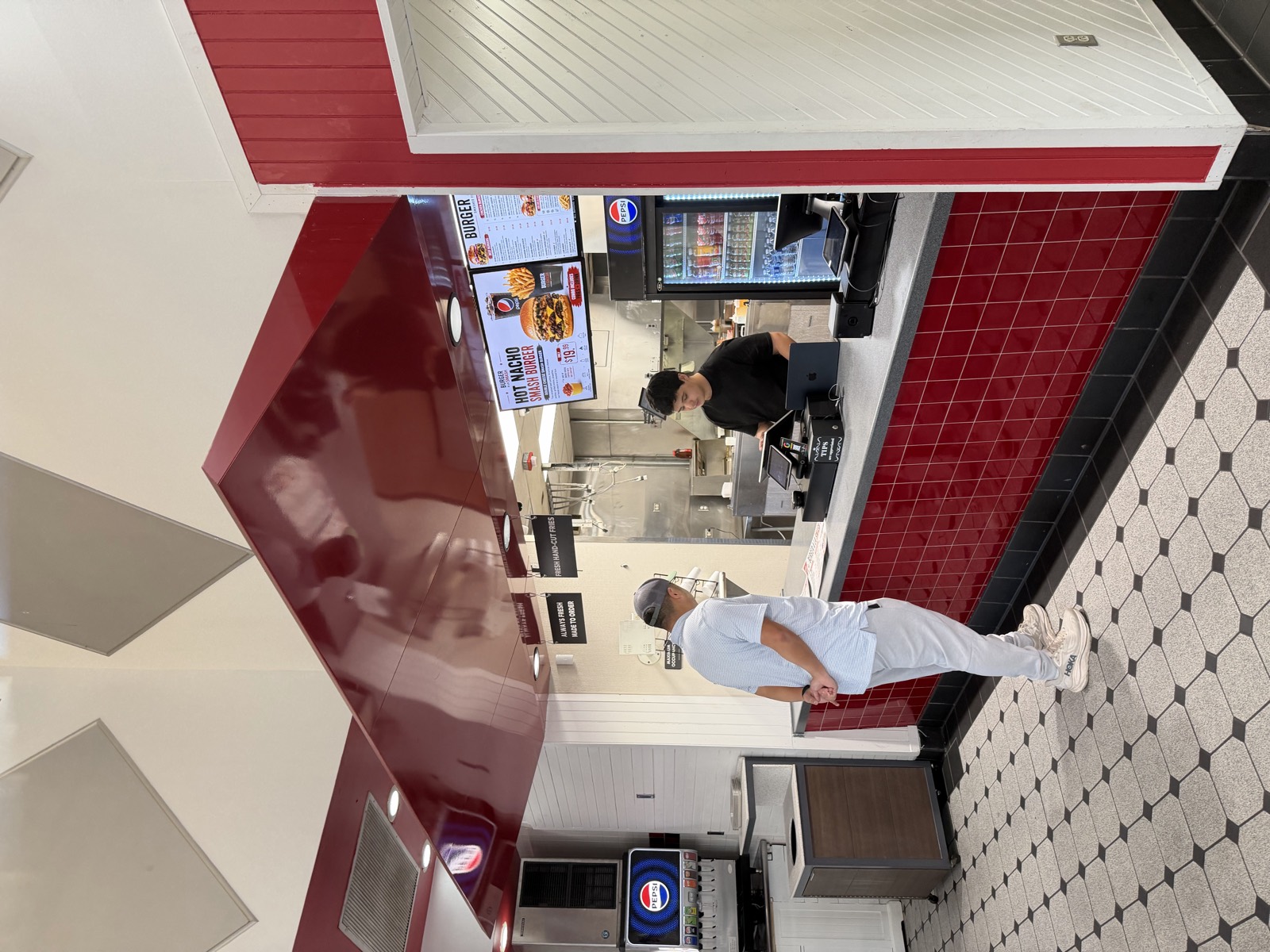 The order counter inside Burger A La Smash, with red tile, checkerboard floor and menu screens above the kitchen