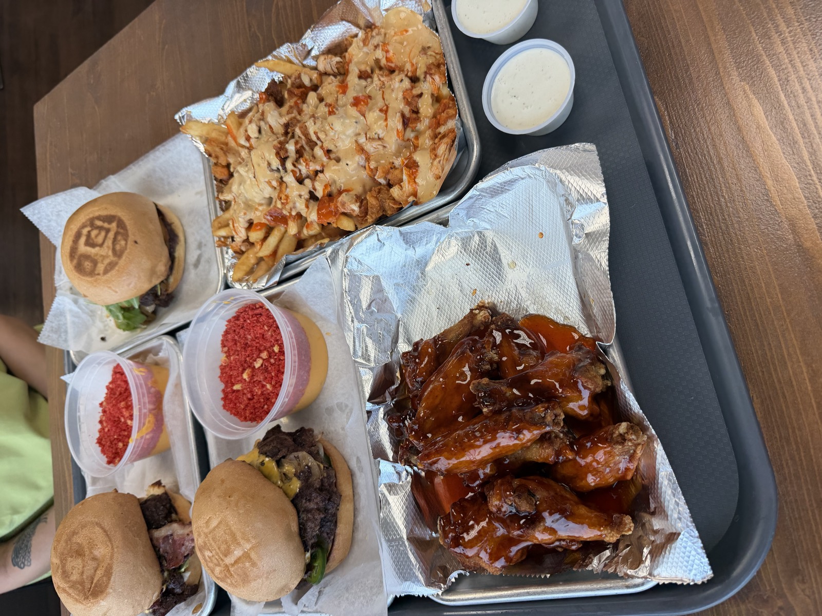 Sam's order laid out on a tray: three smash burgers, loaded fries, hot honey wings and two cups of nacho cheese topped with red chip crumbs