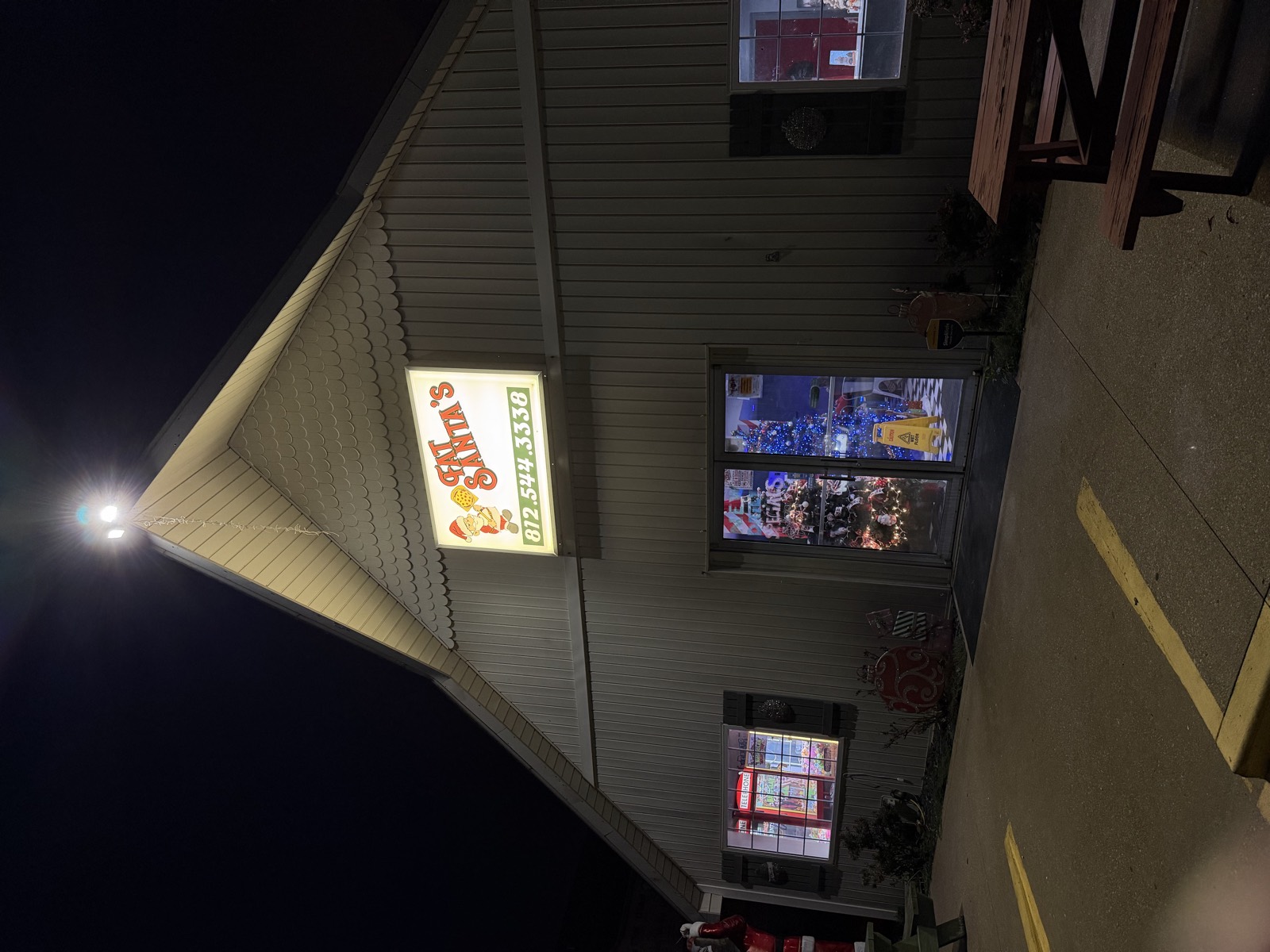 Fat Santa's lit sign on the barn-style building at night, with picnic tables and Christmas decorations out front