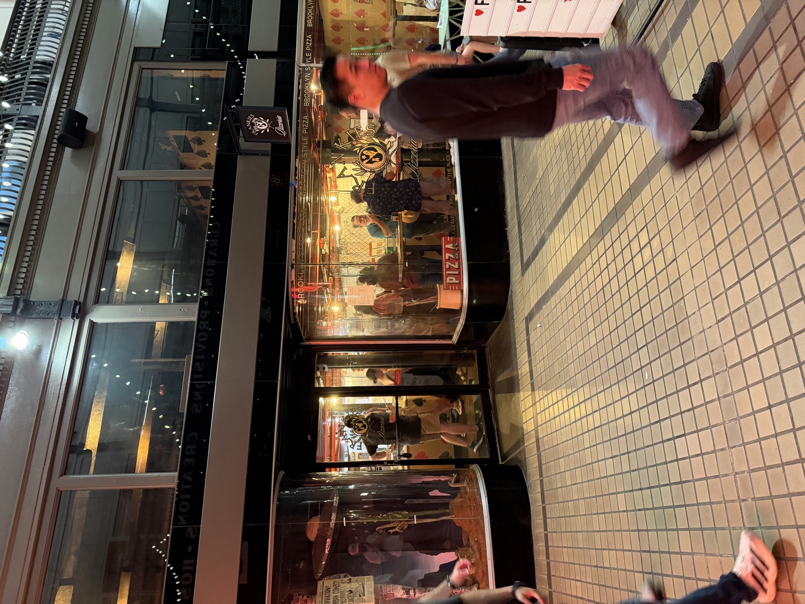Frankies Pizzeria's window inside The Arcade at night, with a Brooklyn Style Pizza sign above the counter