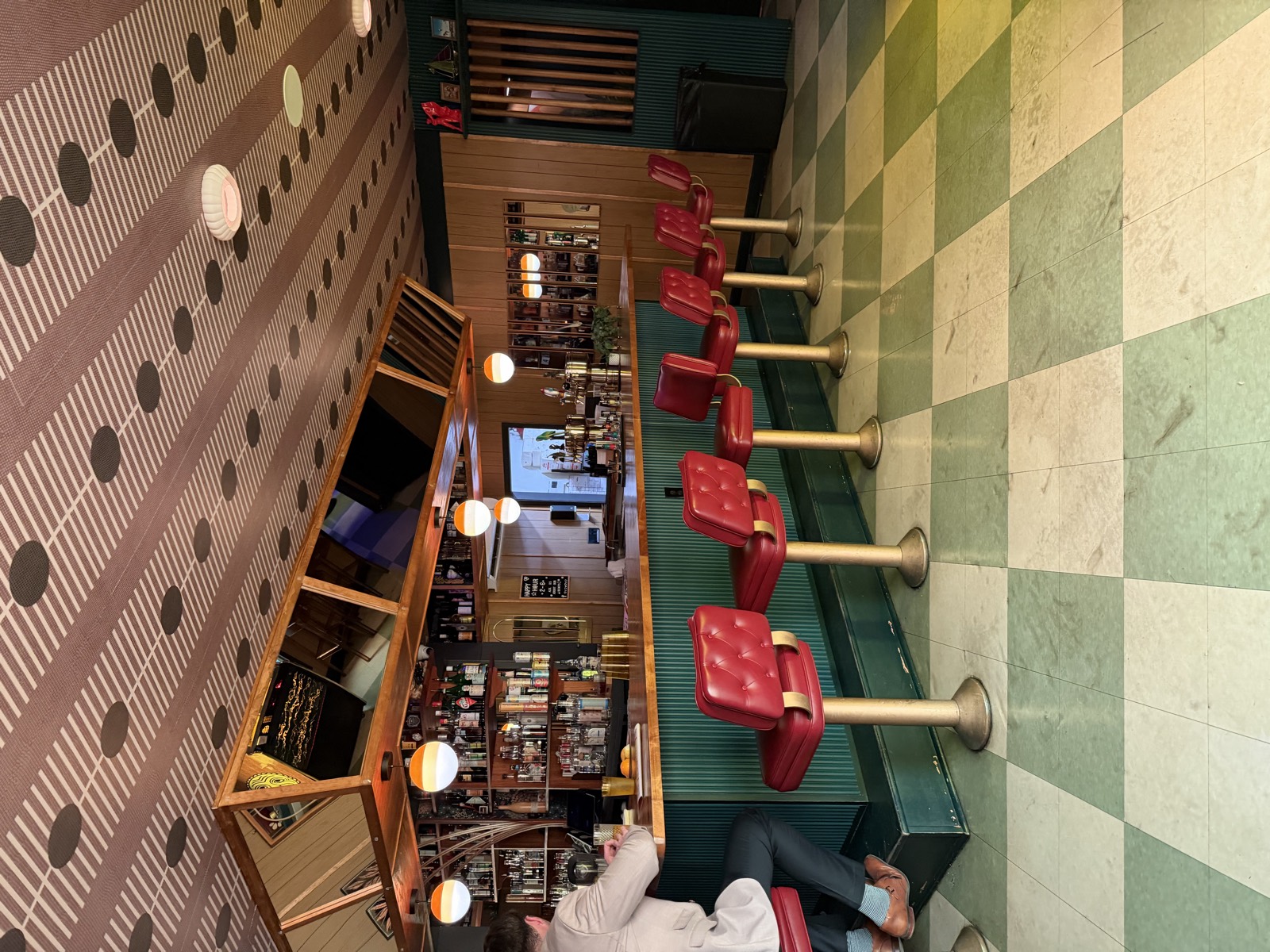 The bar inside GoodTimes, with red vinyl stools, a green checkerboard floor and TVs over the bottles