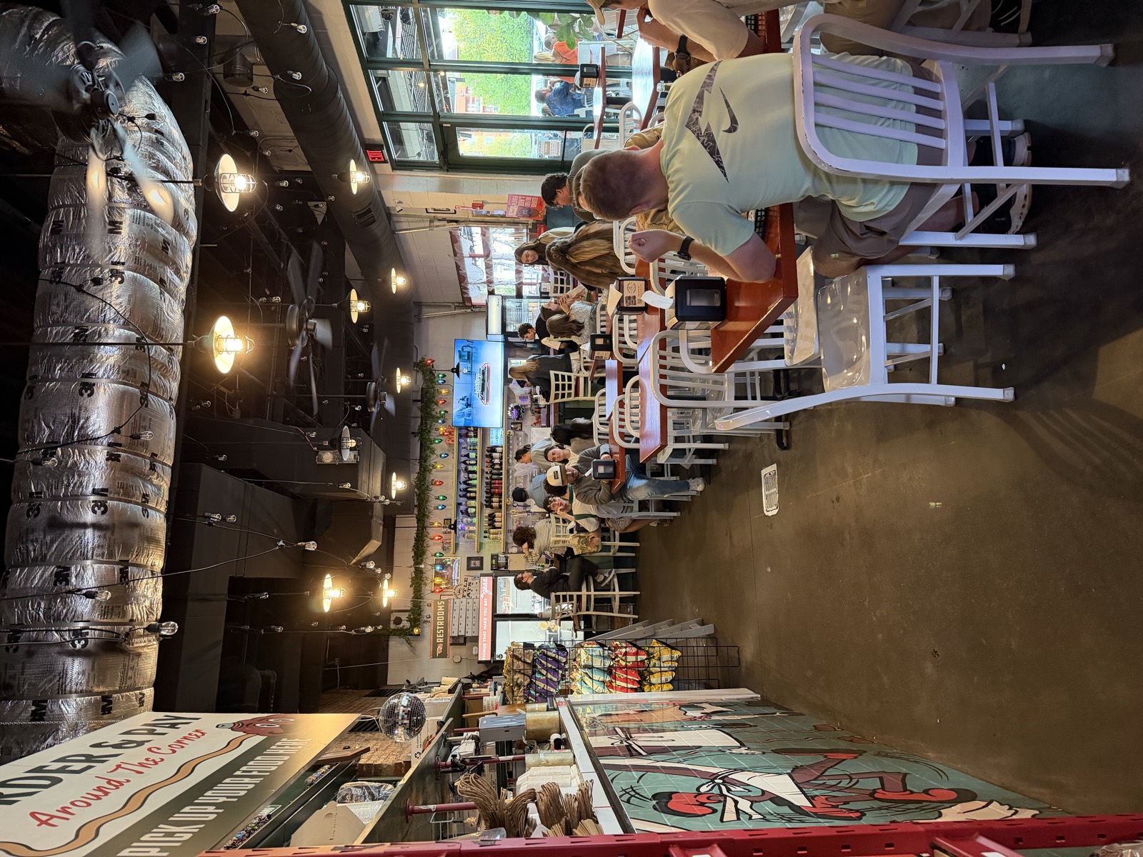 Inside Little Hats, a narrow dining room with white chairs, string lights and shelves of Italian imports along the wall