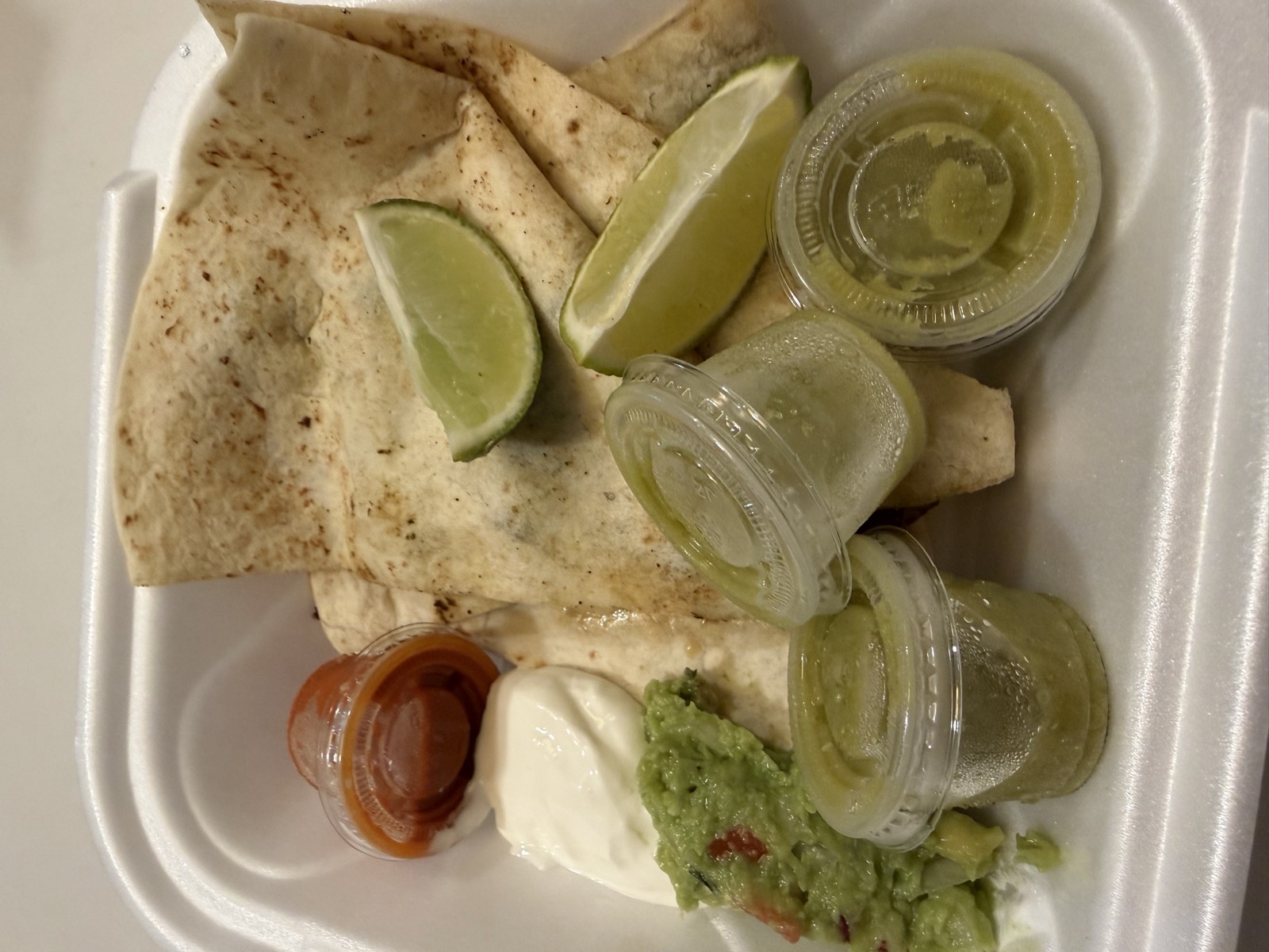Sam's order: the Steak Quesadilla in a takeout container with guacamole, sour cream, salsa and lime