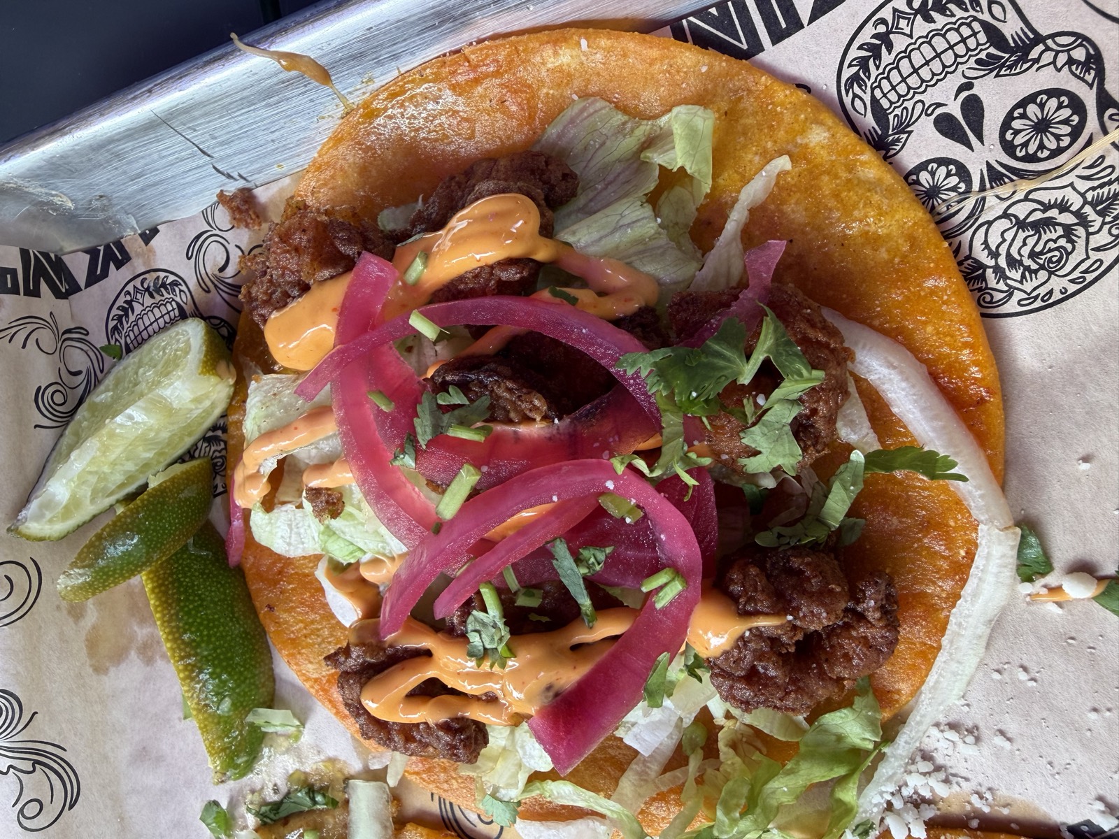 A close-up of one of Sam's tacos, with crispy fried pieces, pickled red onion, lettuce and a chipotle drizzle